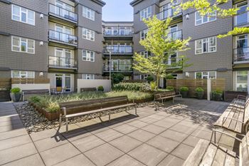 a courtyard with two benches and a tree in front of an apartment building at 128 on State, Kirkland, WA